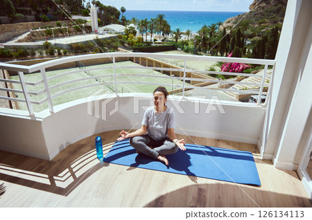 Young Woman Meditating on a Terrace with Scenic Outdoor View 126134113