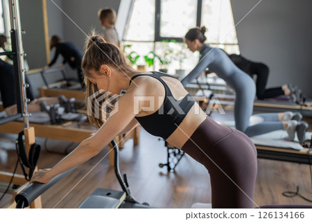Group of caucasian women exercising with trainer on pilates reformers in a bright studio. Their workout focuses on core strength and flexibility in a modern fitness environment 126134166