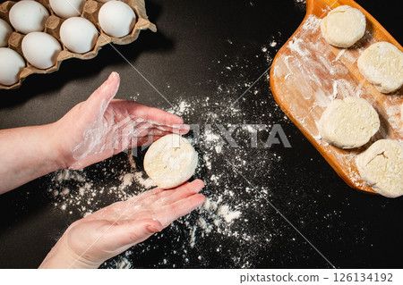 Process of making syrniki. From finished curd dough cut off pieces for future syrniki and form into round. Top view on black surface. Russian cuisine. Process of making syrniki. From finished curd dough cut off pieces for future syrniki and form into round. Top view on black surface. Russian cuisine. 126134192