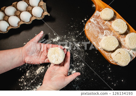 Process of making syrniki. Form round syrniki from curd dough prepare them for baking or frying. Top view on black surface. Russian cuisine. 126134193