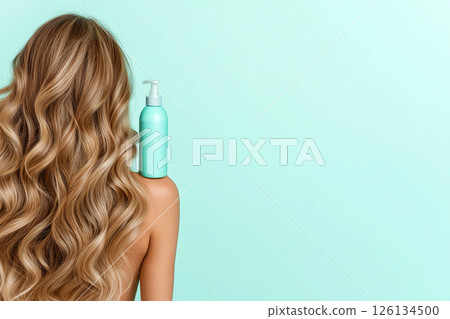 A woman displaying her long, wavy, blonde hair with a focus on a blue shampoo bottle, illustrating clean and healthy hair care enhancing beauty. 126134500