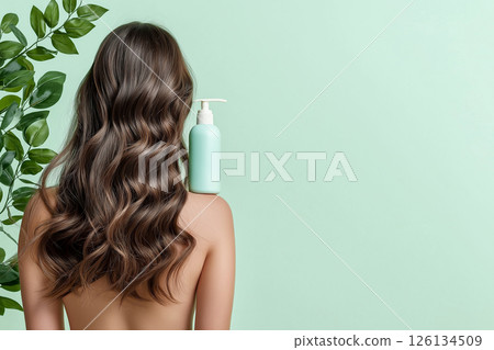 A woman showcasing her lustrous, wavy hair demonstrates a haircare product's versatility. The blue shampoo bottle on her shoulder emphasizes beauty, radiance, and healthy hair. Self-care and grooming. 126134509