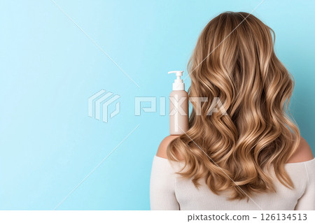 A woman showcasing her lustrous, wavy hair demonstrates a haircare product's versatility. The blue shampoo bottle on her shoulder emphasizes beauty, radiance, and healthy hair. Self-care and grooming. 126134513