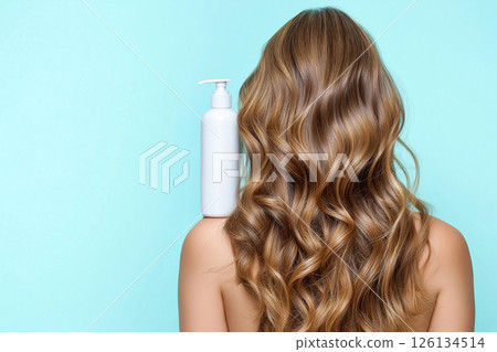 A woman showcasing her lustrous, wavy hair demonstrates a haircare product's versatility. The blue shampoo bottle on her shoulder emphasizes beauty, radiance, and healthy hair. Self-care and grooming. 126134514