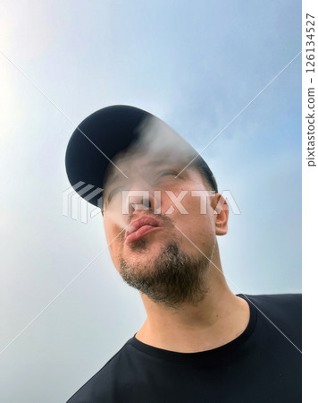 man exhales smoke from vape against fog and smog in nature 126134527