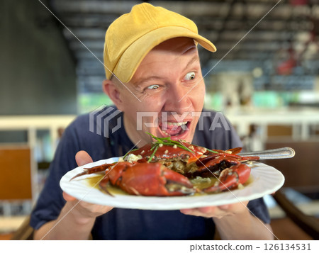 man eating crab, holding crab on plate and trying to bite 126134531