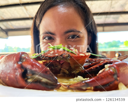 young asian woman showing off crab on plate peeking out from behind crab 126134539