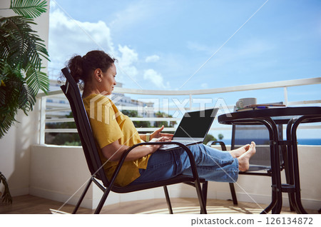 Woman Working Remotely on a Laptop at a Balcony with Ocean View Woman Working Remotely on a Laptop at a Balcony with Ocean View 126134872