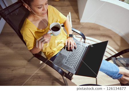 Woman Enjoying Coffee While Using Laptop in Bright Modern Space Woman Enjoying Coffee While Using Laptop in Bright Modern Space 126134877