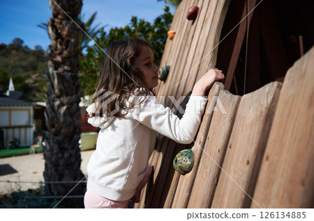 Young Girl Climbs Wooden Rock Wall in Outdoor Park Setting Young Girl Climbs Wooden Rock Wall in Outdoor Park Setting 126134885