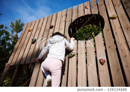 Child Climbing a Wooden Rock Wall Outdoors Beneath a Blue Sky in a Natural Setting Child Climbing a Wooden Rock Wall Outdoors Beneath a Blue Sky in a Natural Setting 126134886