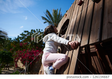 Child Enjoying Outdoor Play Climbing a Wooden Structure on a Bright Day Child Enjoying Outdoor Play Climbing a Wooden Structure on a Bright Day 126134887