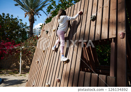 Child Climbing Wooden Rock Wall in Outdoor Playground with Palm Trees Child Climbing Wooden Rock Wall in Outdoor Playground with Palm Trees 126134892