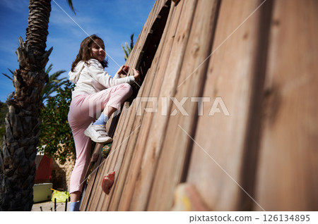 Young Girl Climbing an Outdoor Wooden Wall on a Sunny Day 126134895