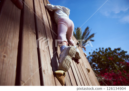 Child Climbing a Wooden Wall Outdoors on a Sunny Day Child Climbing a Wooden Wall Outdoors on a Sunny Day 126134904