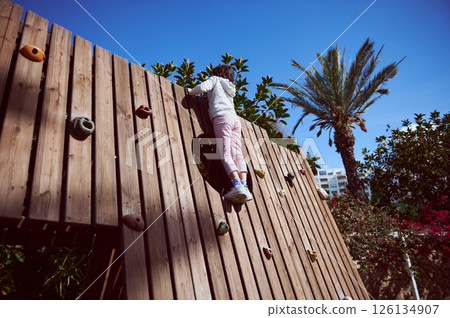 Child Climbing a Wooden Wall Outdoors on a Sunny Day in Nature Child Climbing a Wooden Wall Outdoors on a Sunny Day in Nature 126134907
