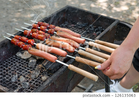 female hand frying sausages on skewers on grill 126135063