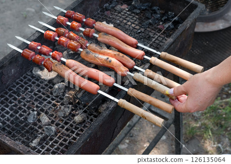female hand frying sausages on skewers on grill female hand frying sausages on skewers on grill 126135064