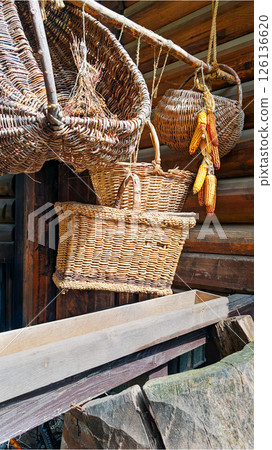 Wicker baskets and dried corn hanging on wooden wall, rustic countryside still life in sunlight Wicker baskets and dried corn hanging on wooden wall, rustic countryside still life in sunlight 126136620