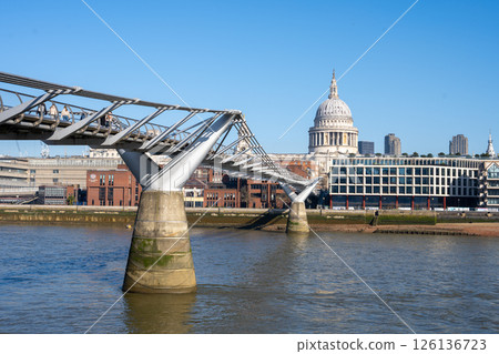 A clear blue sky creates a stunning backdrop as the Millennium Bridge stretches over the River Thames, leading to the iconic St. Paul's Cathedral. Visitors stroll along its pathway. A clear blue sky creates a stunning backdrop as the Millennium Bridge stretches over the River Thames, leading to the iconic St. Paul's Cathedral. Visitors stroll along its pathway. 126136723