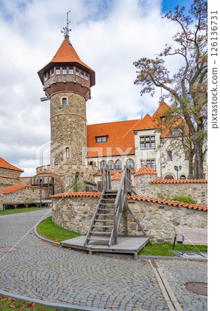 Hnevin Castle, with its distinctive towers and red rooftops, showcases a blend of history and architecture. The cobbled path invites visitors to explore its fascinating surroundings. Hnevin Castle, with its distinctive towers and red rooftops, showcases a blend of history and architecture. The cobbled path invites visitors to explore its fascinating surroundings. 126136731