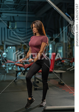 woman performs a workout routine at the gym using a cable machine to strengthen her arms and upper body. She is focused and determined showcasing dedication to fitness. 126137167
