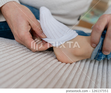 Dad slowly pulls down and pulls the white socks off the baby's feet. High quality photo 126137351