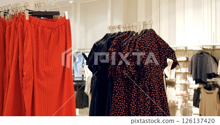 Multiple red pants and black shirts with red polka dots hang on clothing racks in a retail store, creating a visually appealing display for shoppers. Concept fashion clothes 126137420