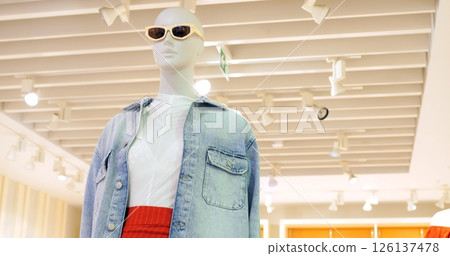 Stylish mannequin displays current fashion trends, showcasing a denim jacket, white shirt, and a vibrant red skirt in a brightly lit retail environment. Concept fashion clothes Stylish mannequin displays current fashion trends, showcasing a denim jacket, white shirt, and a vibrant red skirt in a brightly lit retail environment. Concept fashion clothes 126137478