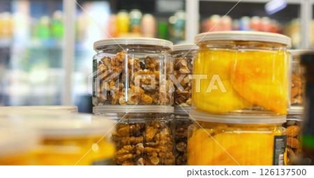 Walnuts and dried mango slices are displayed in clear jars on a supermarket shelf, offering a healthy and convenient snack option for customers Walnuts and dried mango slices are displayed in clear jars on a supermarket shelf, offering a healthy and convenient snack option for customers 126137500