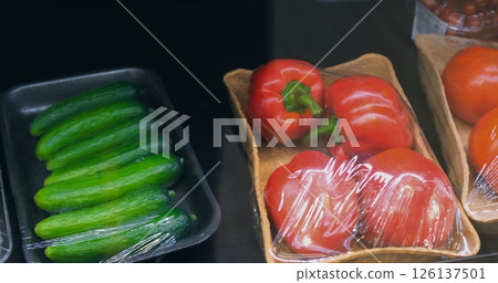 Fresh vegetables wrapped in plastic film displayed on refrigerated supermarket shelf, including cucumbers, bell peppers, and broccoli box highlighting produce freshness and food preservation Fresh vegetables wrapped in plastic film displayed on refrigerated supermarket shelf, including cucumbers, bell peppers, and broccoli box highlighting produce freshness and food preservation 126137501