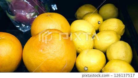 Ripe grapefruits and lemons slowly rotating on black display shelf, showcasing vibrant citrus fruits within fresh produce section of grocery store market 126137517