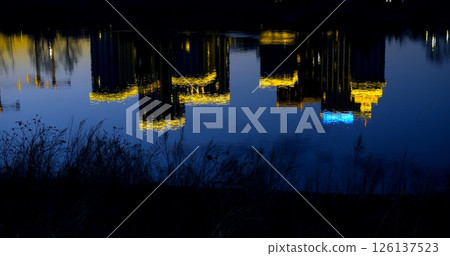 Urban skyline mirroring on a tranquil body of water at night, creating a captivating symmetrical view of illuminated buildings and their reflections 126137523