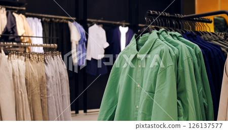 Green shirts hanging tightly packed on clothing rack within retail space, surrounded by diverse garments showcasing fashion variety and store merchandise collection. Concept fashion clothes 126137577