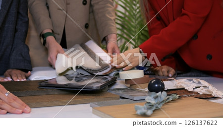 Interior design professionals collaborating at table, reviewing wood, fabric, and tile samples while planning comprehensive renovation strategy. Selection of materials for interior design 126137622