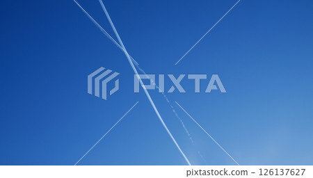 Jet leaving white contrail streaking across pristine blue sky, wispy clouds scattered beneath bright daytime expanse suggesting aerial journey and freedom Jet leaving white contrail streaking across pristine blue sky, wispy clouds scattered beneath bright daytime expanse suggesting aerial journey and freedom 126137627