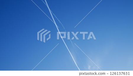 Commercial passenger airplanes cruising at high altitude, creating intersecting white contrails against pristine clear blue sky during daytime flight 126137631