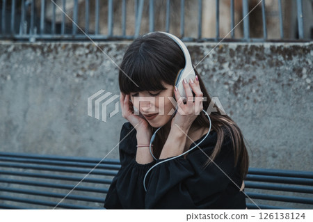 Young Woman Sitting In The City Bench Outdoor And Relaxing With Music  126138124