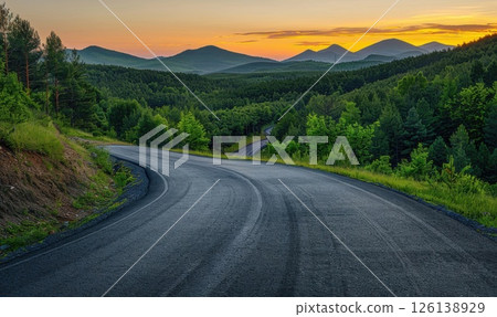 The asphalt road meanders through the forest, leading to distant peaks, while the sunset casts warm orange and pink tones across the sky. The asphalt road meanders through the forest, leading to distant peaks, while the sunset casts warm orange and pink tones across the sky. 126138929