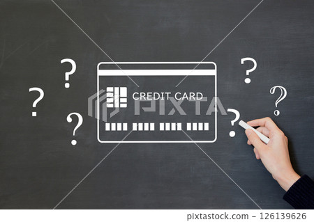A man's hand drawing a credit card icon and various question marks on a blackboard 126139626