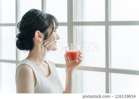 Asian woman drinking red drink in the morning at home (tomato juice, red smoothie, acerola juice) 126139654