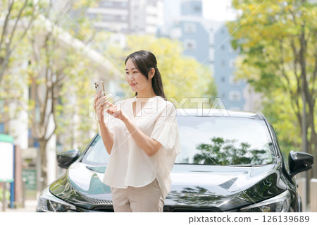 A young woman operating a smartphone in front of a car A young woman operating a smartphone in front of a car 126139689