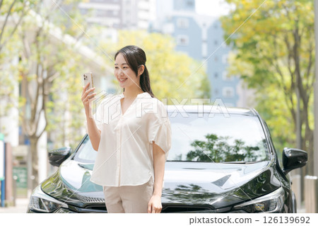 A young woman operating a smartphone in front of a car A young woman operating a smartphone in front of a car 126139692