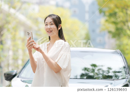 A young woman operating a smartphone in front of a car 126139693