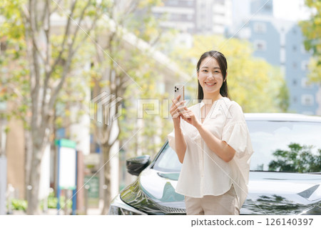 A woman looking at her smartphone in front of a car 126140397