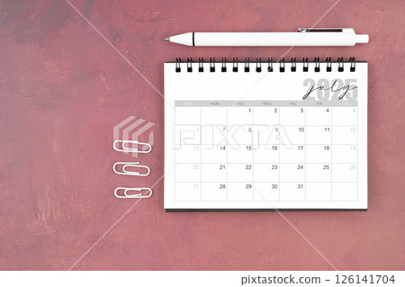 Desk calendar for July 2025 and pen with paper clips on red table. 126141704