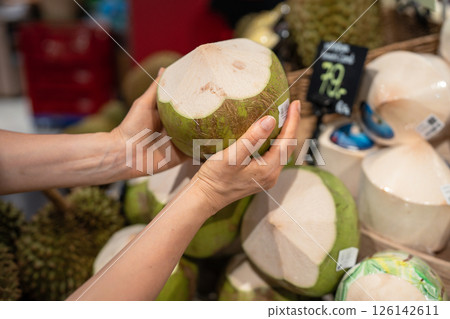 Woman holds green coconut from market stall selecting for milk and dietary use, exotic nut food 126142611