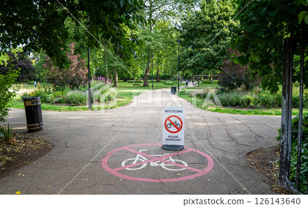 Park pathway with no cycling sign in the center. Surrounded by green trees flowers and walking area. Park pathway with no cycling sign in the center. Surrounded by green trees flowers and walking area. 126143640