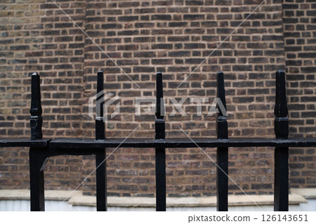 Close view of a black iron fence with pointed tops in front of an old brick wall. Close view of a black iron fence with pointed tops in front of an old brick wall. 126143651