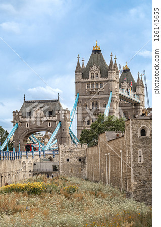 Tower Bridge rises behind the weathered stone walls of the Tower of London, linking past and present across the skyline. 126143655